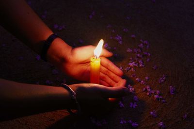 Close-up of hand shielding lit candle by purple flowers