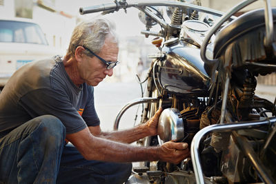 Side view of senior man repairing motorcycle outdoors