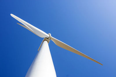 Looking up at wind turbine against blue sky