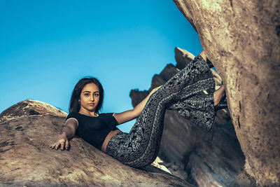 Portrait of woman sitting on rock against sky