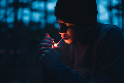 Young boy 19-20 year old smoking cigarette at night outdoors closeup. dark noisy picture.