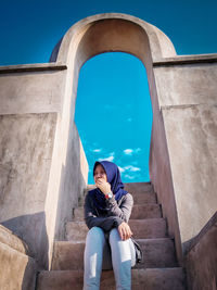 Full length portrait of woman sitting against blue sky