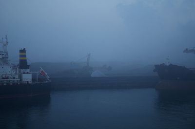 Boats moored at harbor against sky during foggy weather