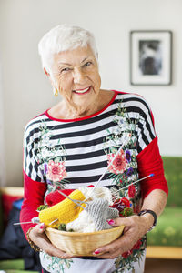 Portrait of happy senior woman holding knitting basket at nursing home