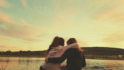 Lesbian couple with arm around sitting at lakeshore