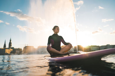 Young woman looking at city against sky during sunset