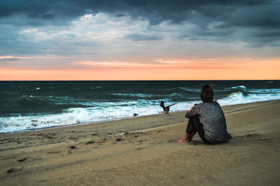Rear view of woman sitting on beach watching ocean sunrise dark clouds
