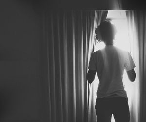 Rear view of man looking through window at home