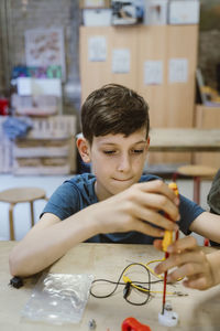 Boy tightening screw on electrical part using screwdriver on table at workshop in school