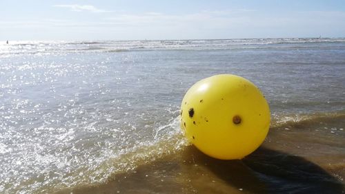 Yellow ball in sea against sky