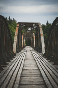 Empty footbridge amidst trees against sky