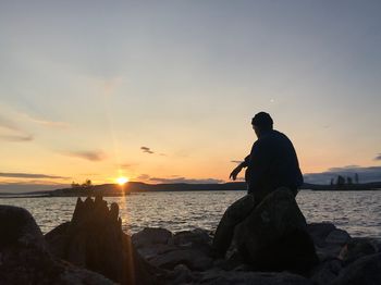 Silhouette man on rock at beach against sky during sunset