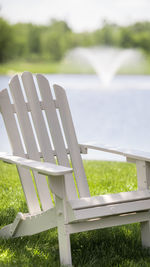 Close-up of a white adirondack chair in the grass, by a lake