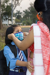 An indian school girl child going to school again after pandemic with her mother wearing mask 