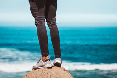 Low section of man standing on rock over sea