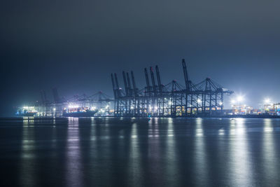 Cranes at harbor against sky at night