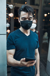 Young man wearing mask using smart phone outdoors