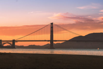 Suspension bridge over river against sky during sunset