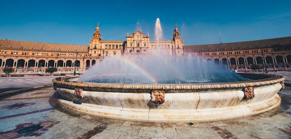 Fountain in front of building against blue sky