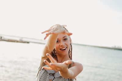 Close-up portrait of smiling young woman gesturing against lake