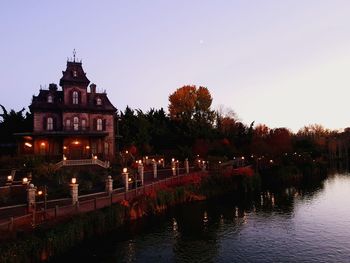 Illuminated building by lake against sky