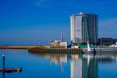 Buildings by river against blue sky