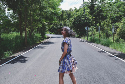 Woman standing on road amidst trees in city