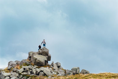 Low angle view of couple on rock formation against cloudy sky