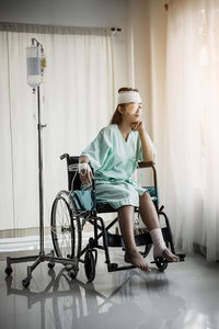 Woman with physical injury sitting on wheelchair by iv drip at hospital