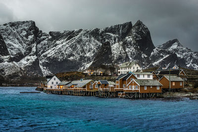 Built structure by sea against sky - reine norway in winter