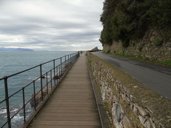 Walkway by sea against sky