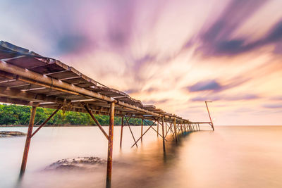 Metallic structure by sea against sky during sunset