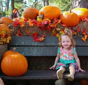 Girl smiling on bench by pumpkins at park during autumn