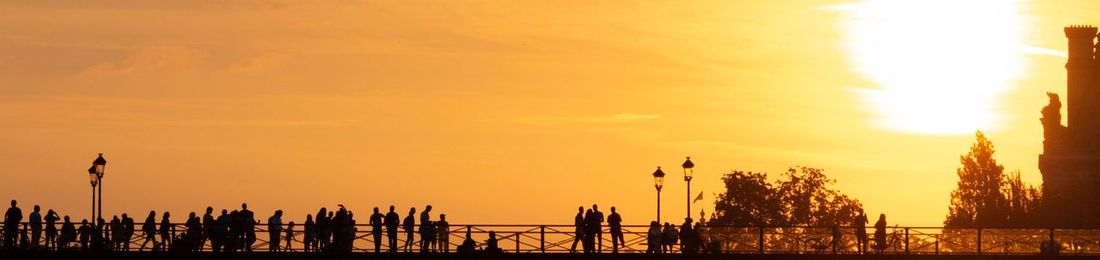 Silhouette people by sea against sky during sunset