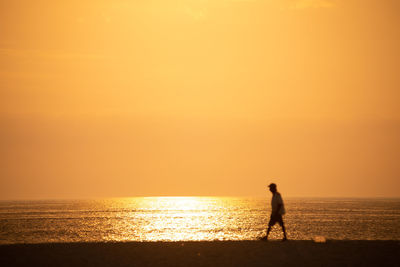 Silhouette woman walking at beach against orange sky