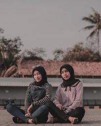 Friends sitting on road against sky