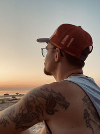 Side view of young man wearing hat against clear sky