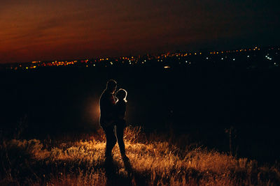 People standing on illuminated field against sky at night