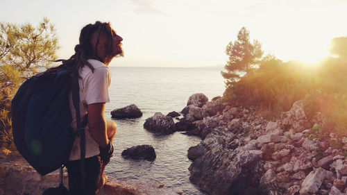 Side view of man standing by sea during sunset