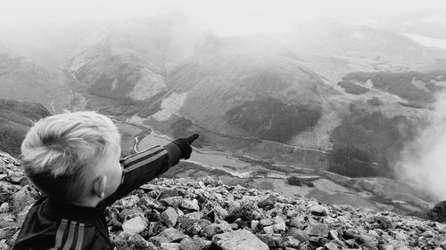 Boy pointing towards mountain during foggy weather