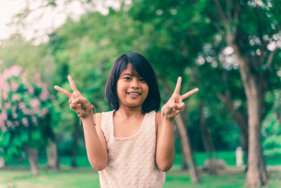 Portrait of smiling girl gesturing peace sign while standing at park