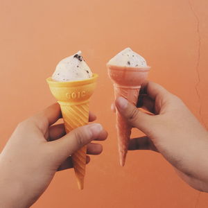 Cropped image of hands holding ice creams against wall