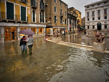 People with umbrellas on water filled walkway during flood at piazza san marco