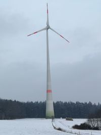 Windmill on snow covered landscape against sky