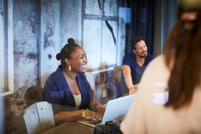 Creative businesswoman smiling while using laptop during meeting with colleagues in office