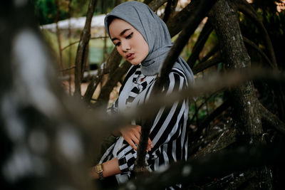 Young woman standing by tree trunk