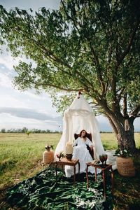 Woman sitting on table against trees on field