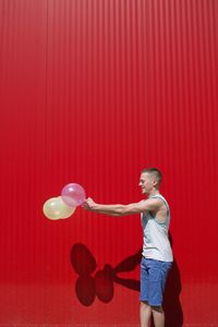 Man holding balloons while standing against red wall