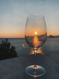 Wineglass on beach against sky during sunset