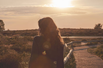 Rear view of woman standing on field against sky during sunset